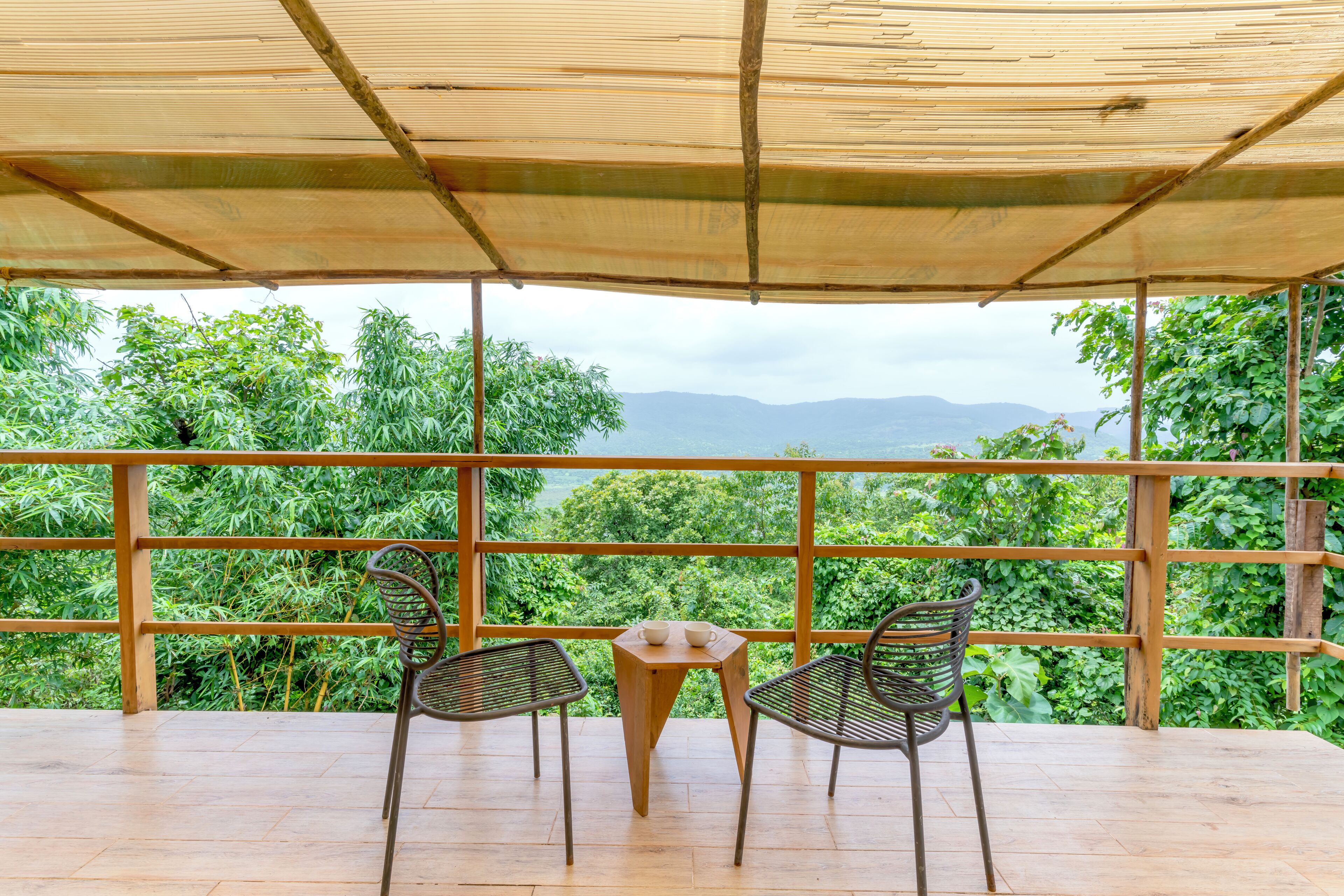 Een overdekt terras met een tafel en twee stoelen, met uitzicht op een weelderig groen landschap met bergen in de verte.