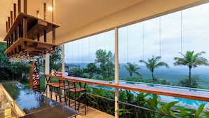 A modern outdoor bar area with a pool view, wooden furniture, and a hanging light fixture. - Forest Hills at Tala (Tala)