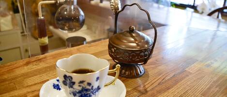 A cup of coffee on a wooden table with a decorative metal container beside it.