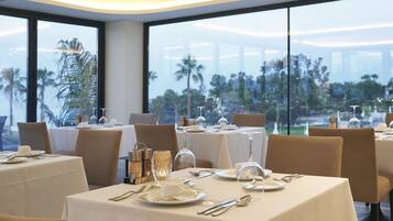 A dining area with tables set for a meal, large windows offering a view of palm trees and a cityscape.