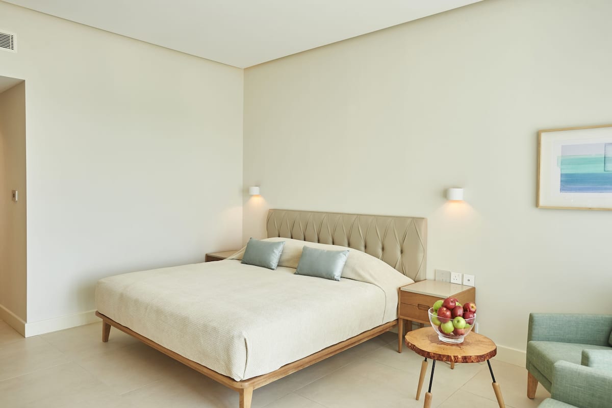 A neatly arranged bedroom with a bed, bedside table, and a small round table with a bowl of fruit.