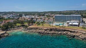 A coastal town with clear turquoise waters, a large modern hotel, and residential buildings. - Sunrise Jade - Adults Only (Paralimni)