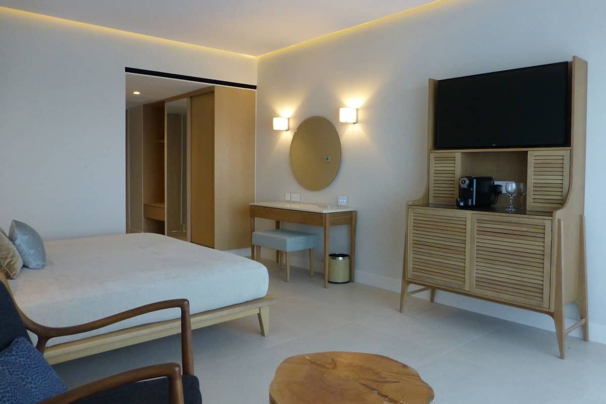 A modern hotel room with a bed, a desk, a mirror, and a television.
