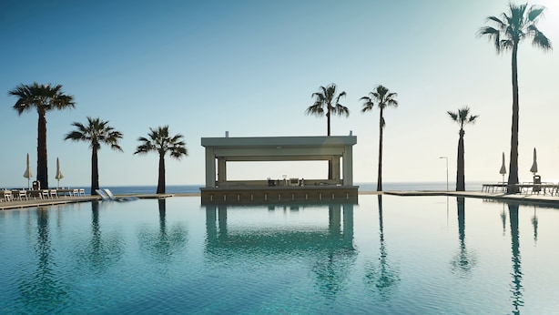 A clear blue pool with lounge chairs and umbrellas, surrounded by palm trees, and a covered seating area. - Sunrise Jade - Adults Only (Paralimni)