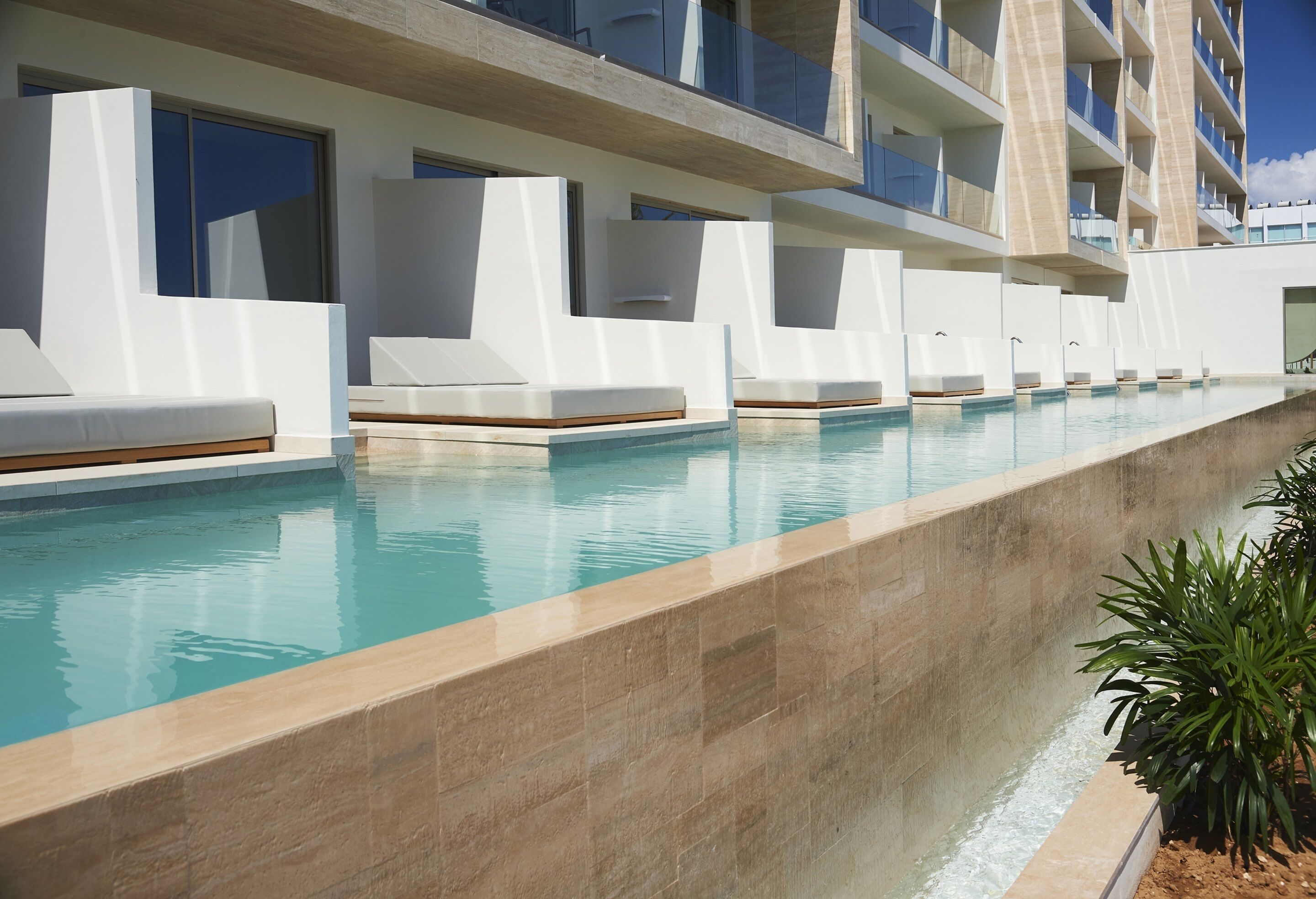 A modern hotel pool area with multiple lounge chairs and a clear view of the building's architecture.
