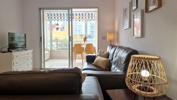 A living room with a leather sofa, a TV on a cabinet, a wicker lamp, and a view of a balcony with chairs. - A37 APOLO 4 ESC 4 4º 16 (Calpe)