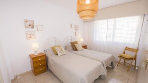 A bedroom with two beds, a wooden nightstand with a lamp, a chair, and a large window with sheer curtains. - A37 APOLO 4 ESC 4 4º 16 (Calpe)