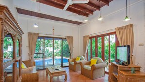 A spacious living room with a pool view, wicker furniture, and a television. - Unique Thai Style 4BR Pool Villa Nikkie (Rawai)