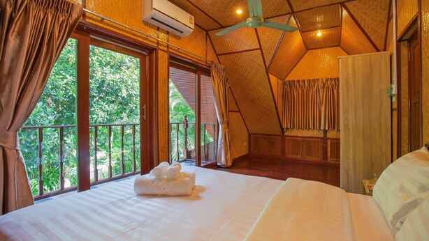 A bedroom with a large bed, an air conditioning unit, a ceiling fan, and a view of greenery outside. - Unique Thai Style 4BR Pool Villa Nikkie (Rawai)