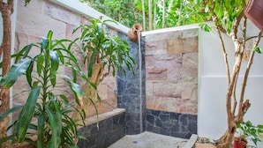 A stone-walled shower area with a built-in water feature, surrounded by lush greenery and potted plants. - Unique Thai Style 4BR Pool Villa Nikkie (Rawai)
