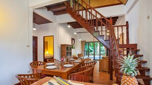 A dining area with a wooden table set for a meal, a wooden staircase, and a fruit bowl on the table. - Unique Thai Style 4BR Pool Villa Nikkie (Rawai)