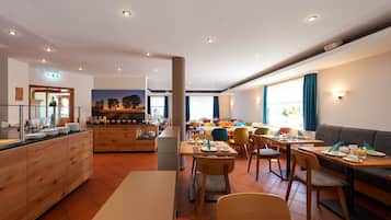 A hotel dining area with multiple tables and chairs, a buffet counter, and a large painting on the wall.