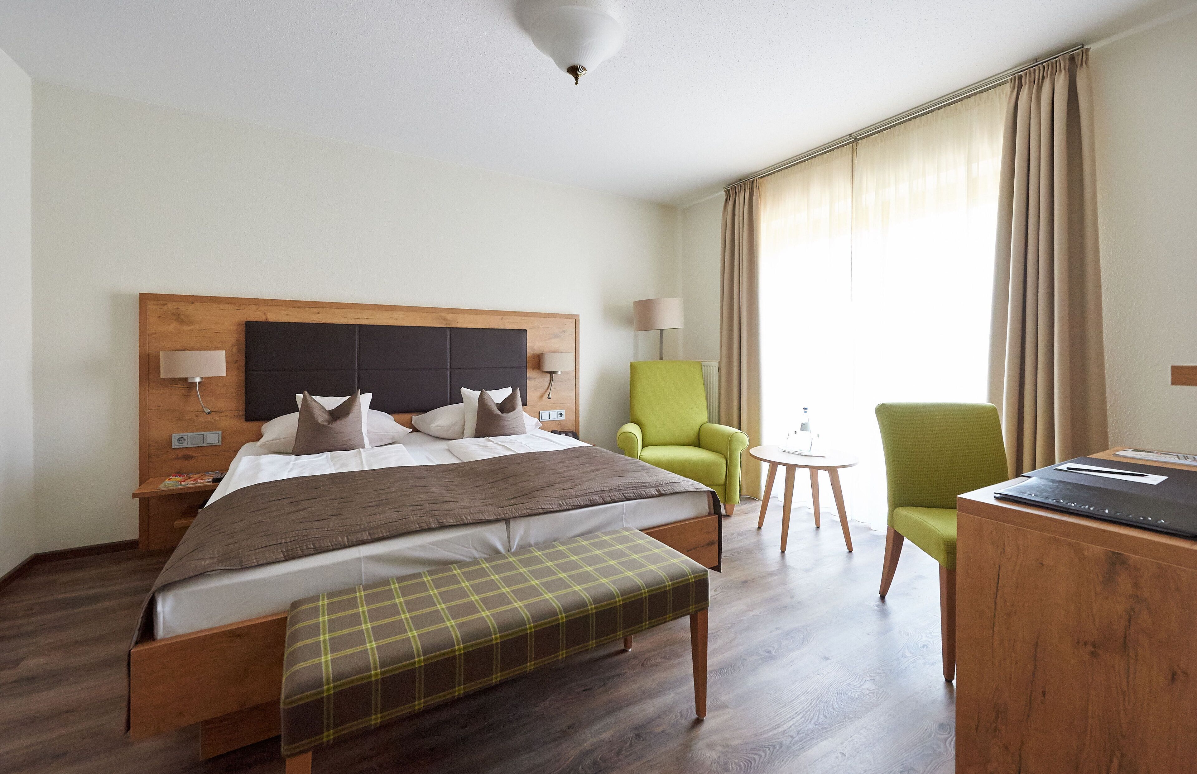 Ein Hotelzimmer mit Bett, Schreibtisch, Stuhl, Lampe und einem Fenster mit Vorhängen.