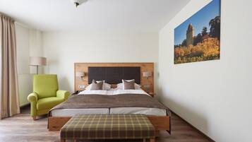 A bedroom with a bed, a green armchair, a bench, a nightstand, a lamp, and a painting on the wall.