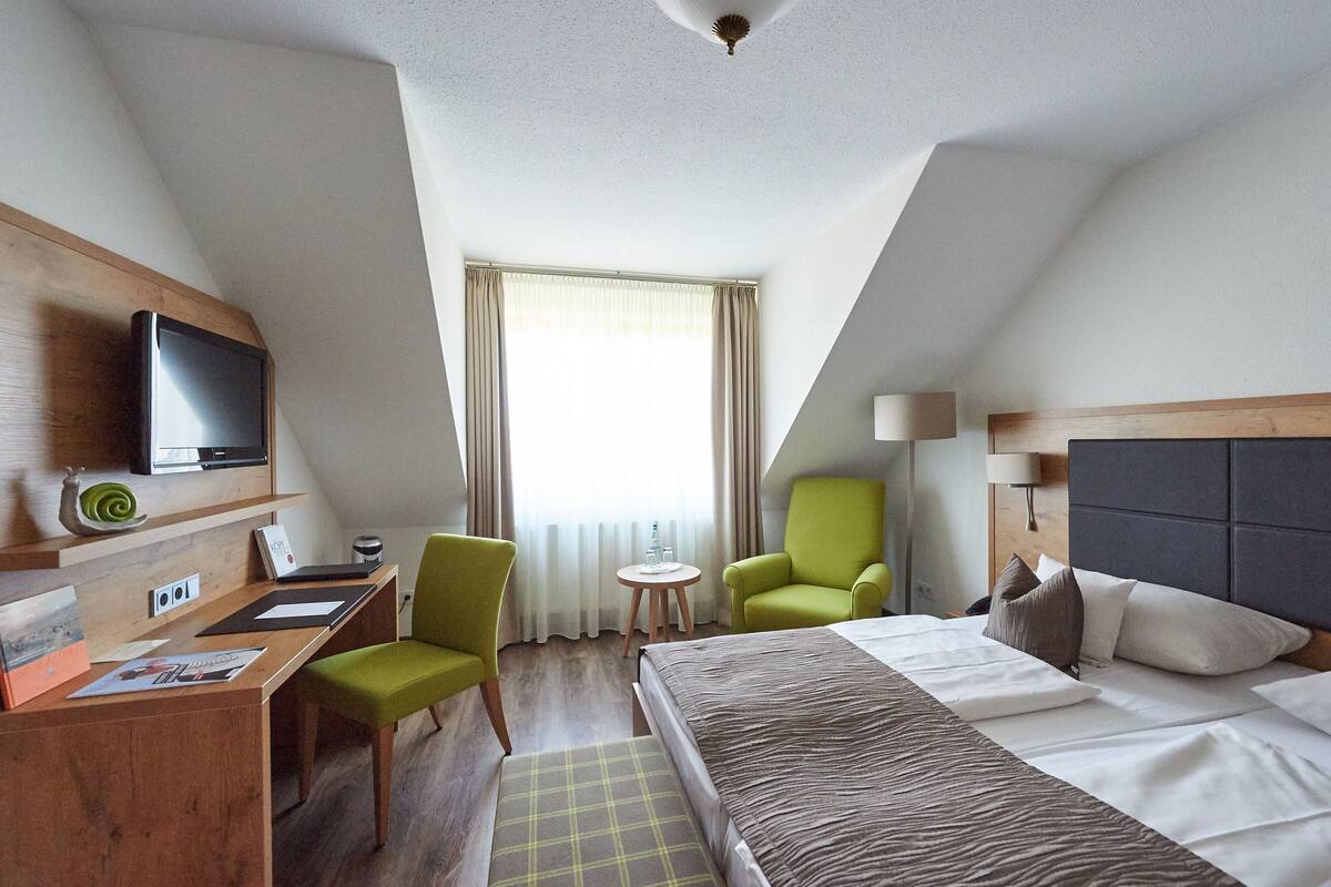 A hotel room with a bed, a desk with a computer, a chair, a television, and a window with curtains.