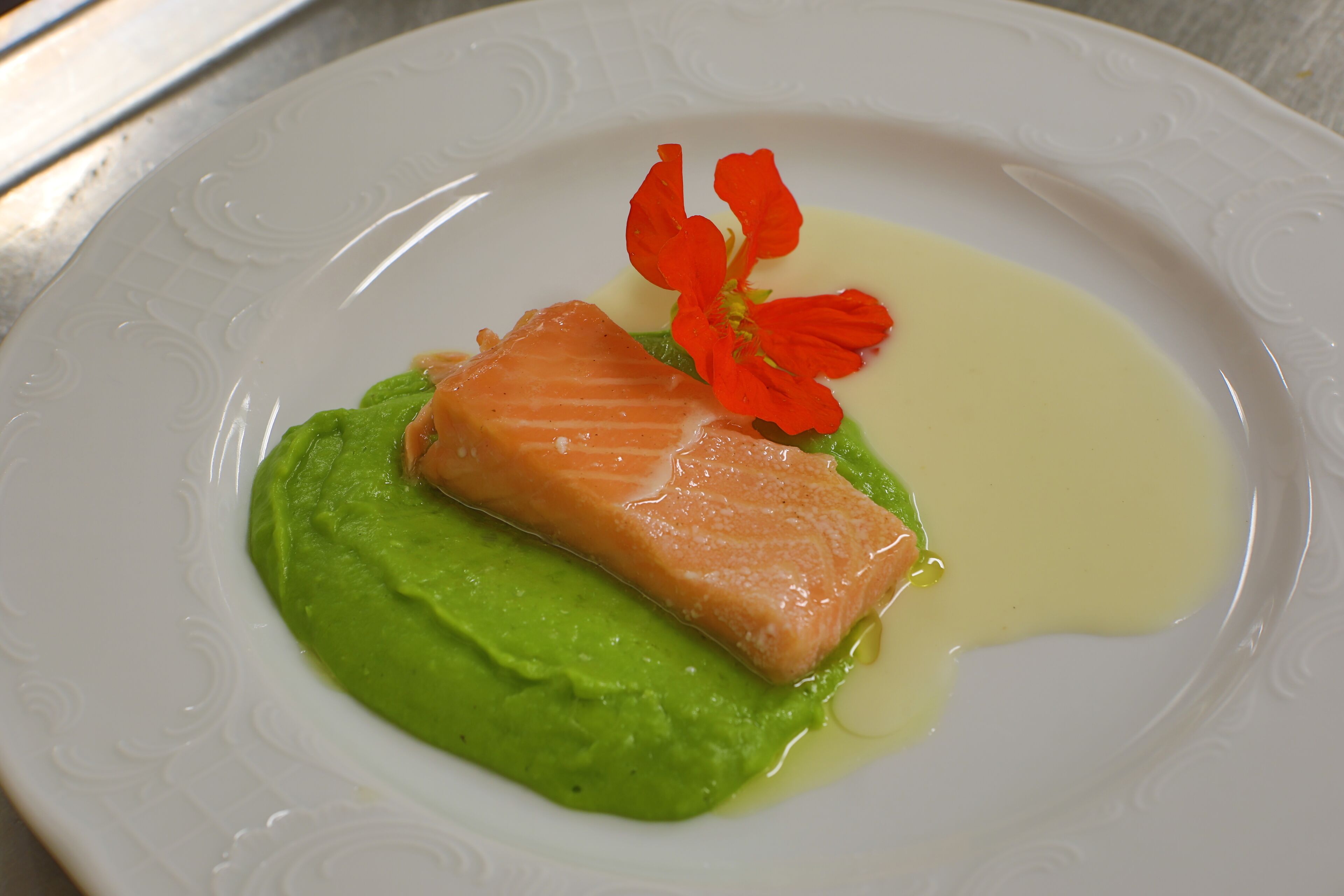 Un plato con salmón, salsa verde y una flor roja como adorno.