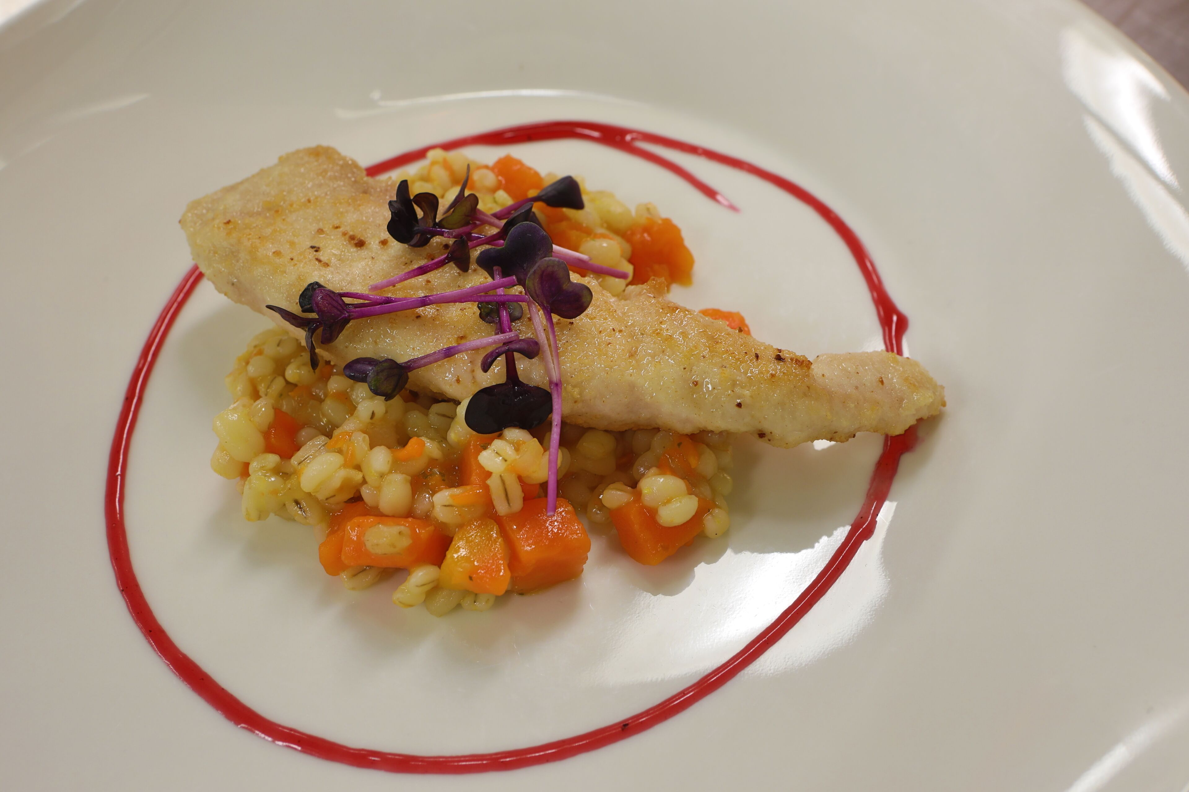 Une assiette blanche contenant un morceau de poisson, un accompagnement à base de céréales et une sauce rouge.