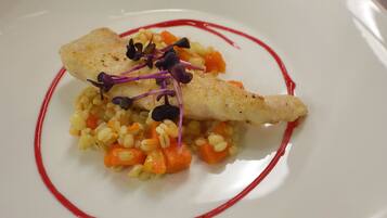 Une assiette blanche contenant un morceau de poisson, un accompagnement à base de céréales et une sauce rouge.