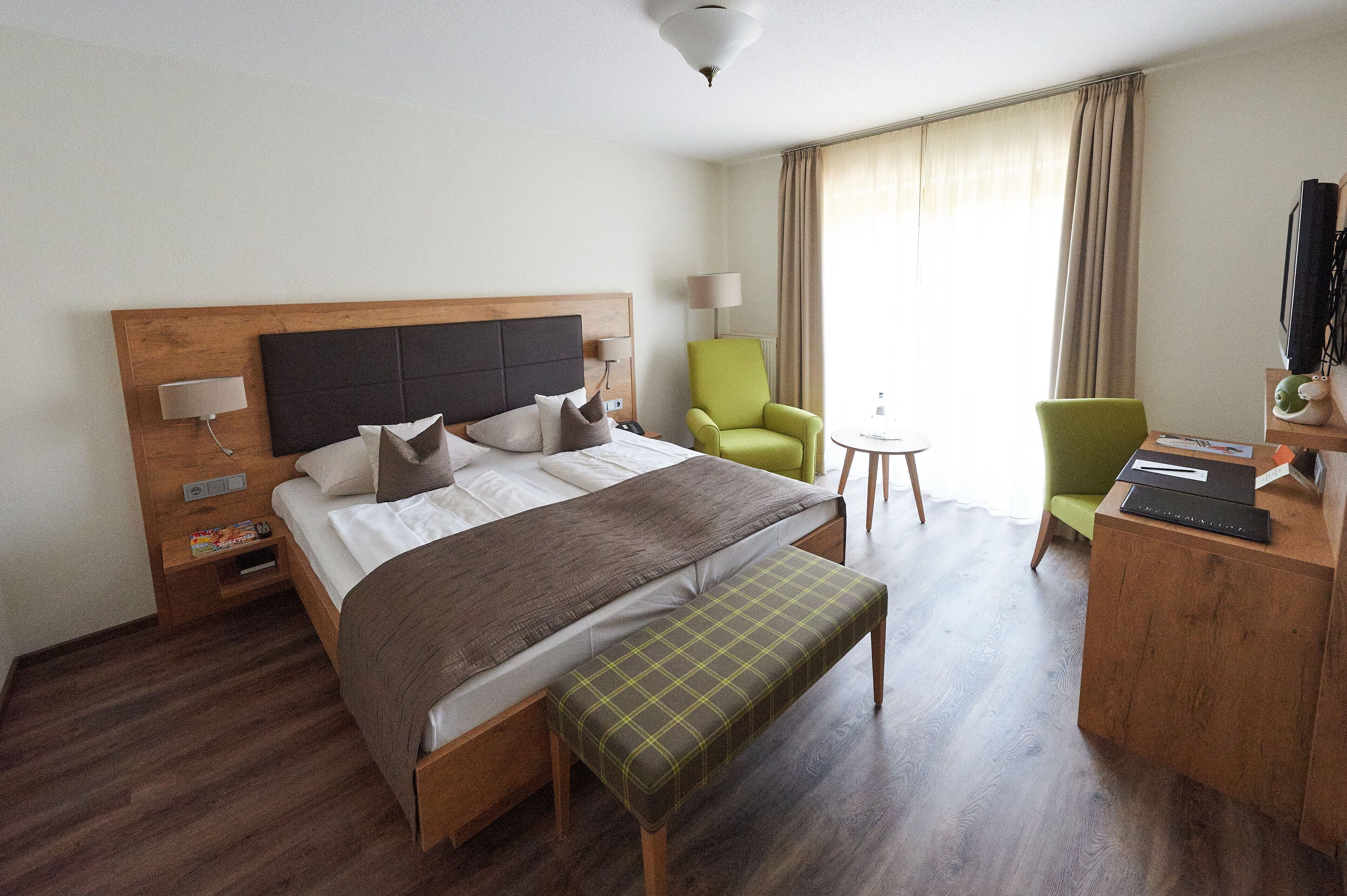 A hotel room with a bed, a desk, a chair, a lamp, and a television.