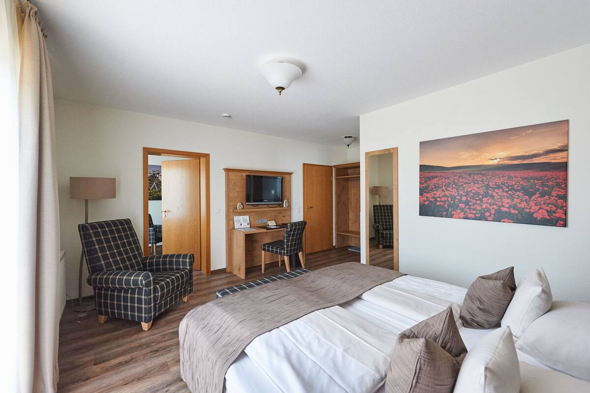 A hotel room with a bed, a desk with a chair, a TV, and a painting of flowers.