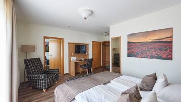 Een hotelkamer met een bed, een bureau met stoel, een televisie en een bloemenstilleven.