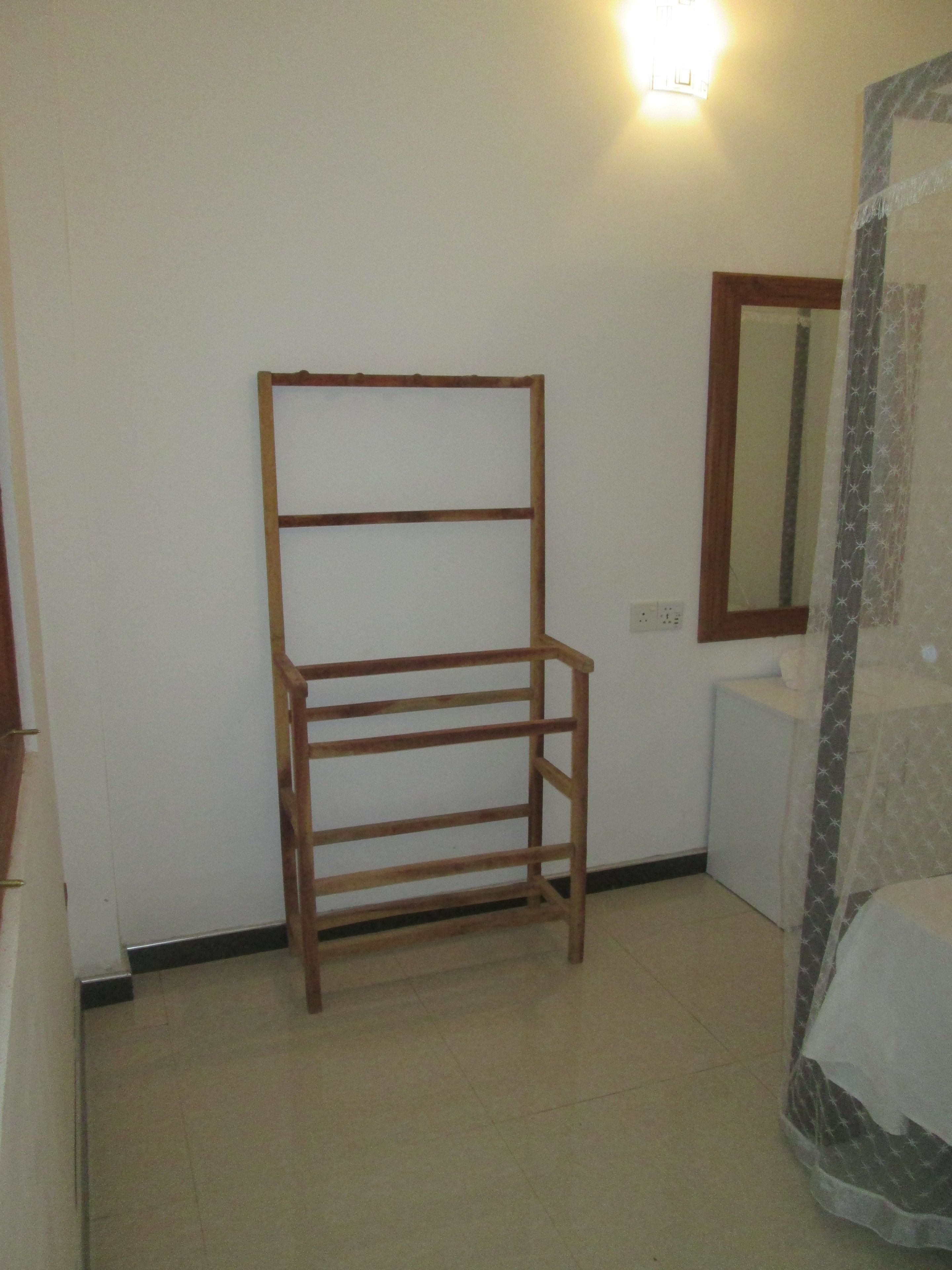 A room with a wooden drying rack, a mirror, and a bed with a patterned curtain.