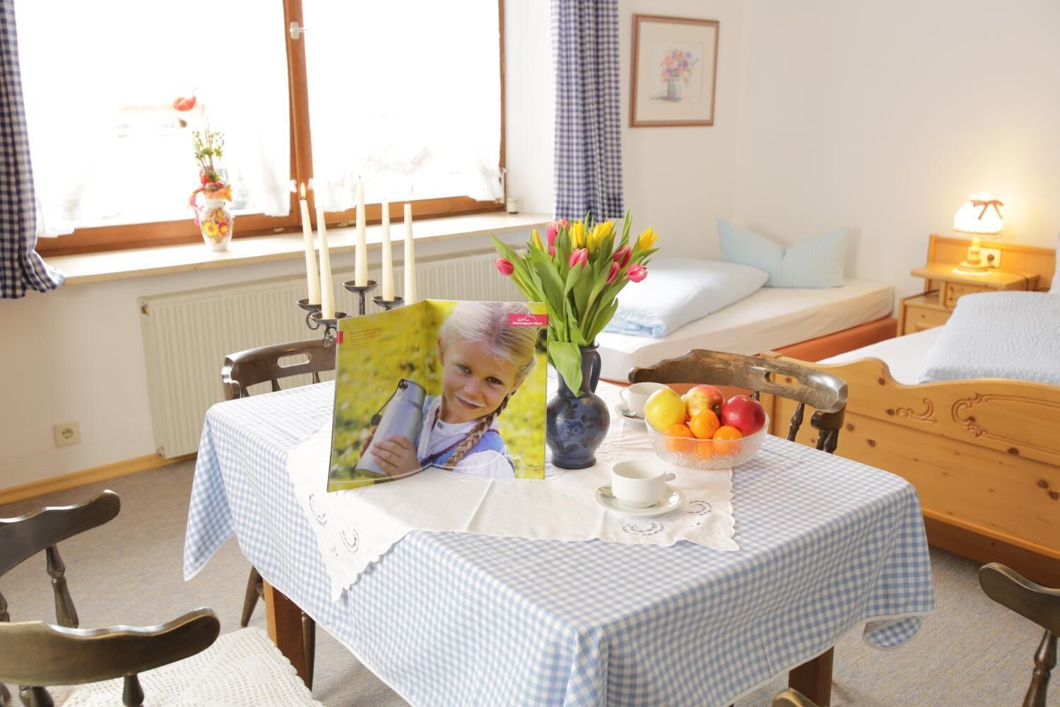 Una habitación acogedora con un mantel a cuadros, una cama con cabecera de madera, una mesita de noche con lámpara y una ventana con cortinas.