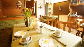 A dining area with a table set for four, including plates, cups, and cutlery. There is a vase with flowers on the table, and a wooden cabinet in the background. - Gästehaus Ethiko (Ettal)