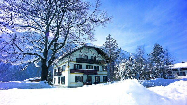 A two-story building with a balcony, surrounded by snow-covered trees and mountains. - Gästehaus Ethiko (Ettal)