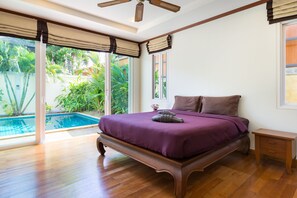 A bedroom with a large bed, wooden flooring, a ceiling fan, and a view of a swimming pool. - Thai Balinese 3BR Pool Villa Alex Rawai (Rawai)
