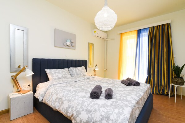 A modern bedroom with a large bed, a bedside lamp, a wall-mounted air conditioner, and a decorative wall piece.