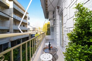 A balcony with a table and chairs, a potted plant, and a view of a multi-story building.