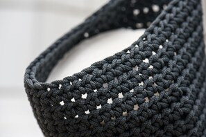 A close-up of a dark, textured, knitted bag with a distinctive pattern and small holes.