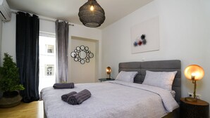 A neatly made bed with grey linens, a bedside lamp, and a decorative wall piece. - A Diamont of 140 m2 Apt (Athens)