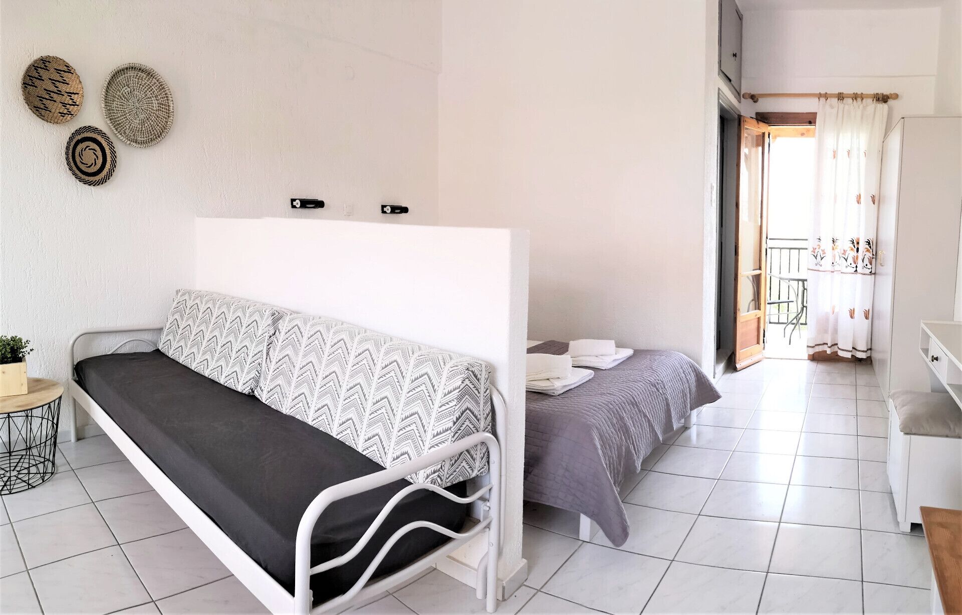 Un dormitorio con cama, sofá, una mesita con una planta y un balcón con vistas.