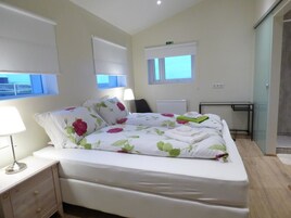 Un dormitorio con cama, mesita de noche, lámpara y vistas al exterior.