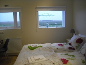A bedroom with a bed, a chair, a window with a view, and a radiator. - 1A Guesthouse (Selfoss)