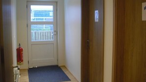 Un pasillo con una puerta marcada '2', un extintor y una ventana con vista a un balcón.