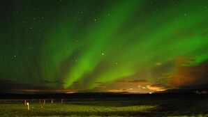 Cielo nocturno con la aurora boreal sobre un paisaje plano y vegetación escasa.