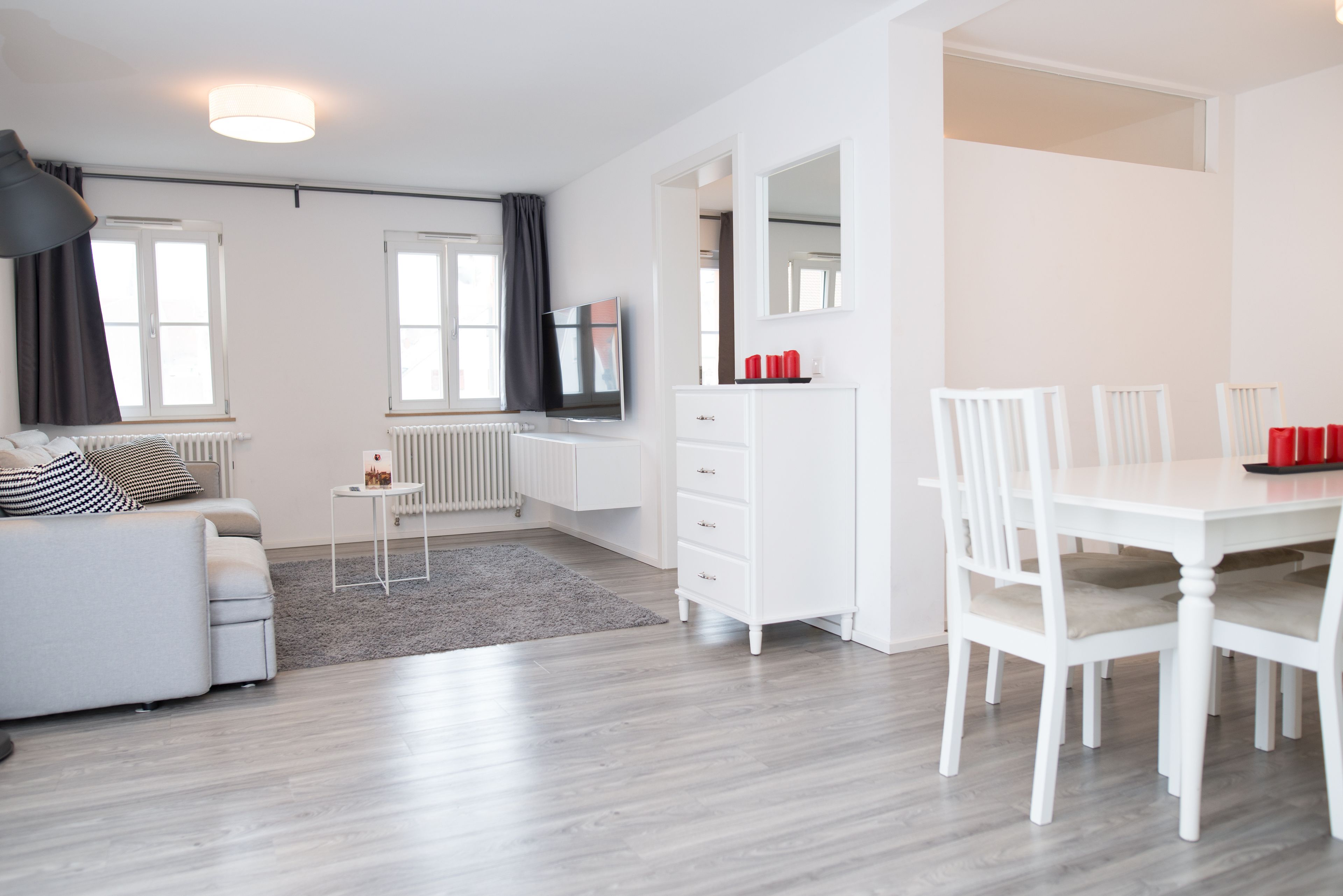 Een moderne woonkamer met een bank, een eettafel met stoelen, een televisie en een witte dressoir.