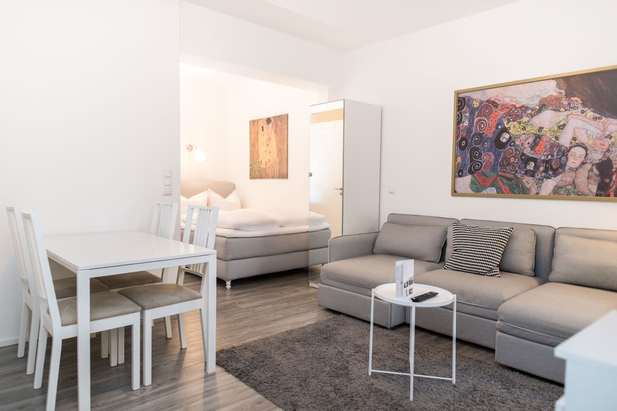 A modern living room with a dining area, a grey sofa, a white table, and a grey rug.