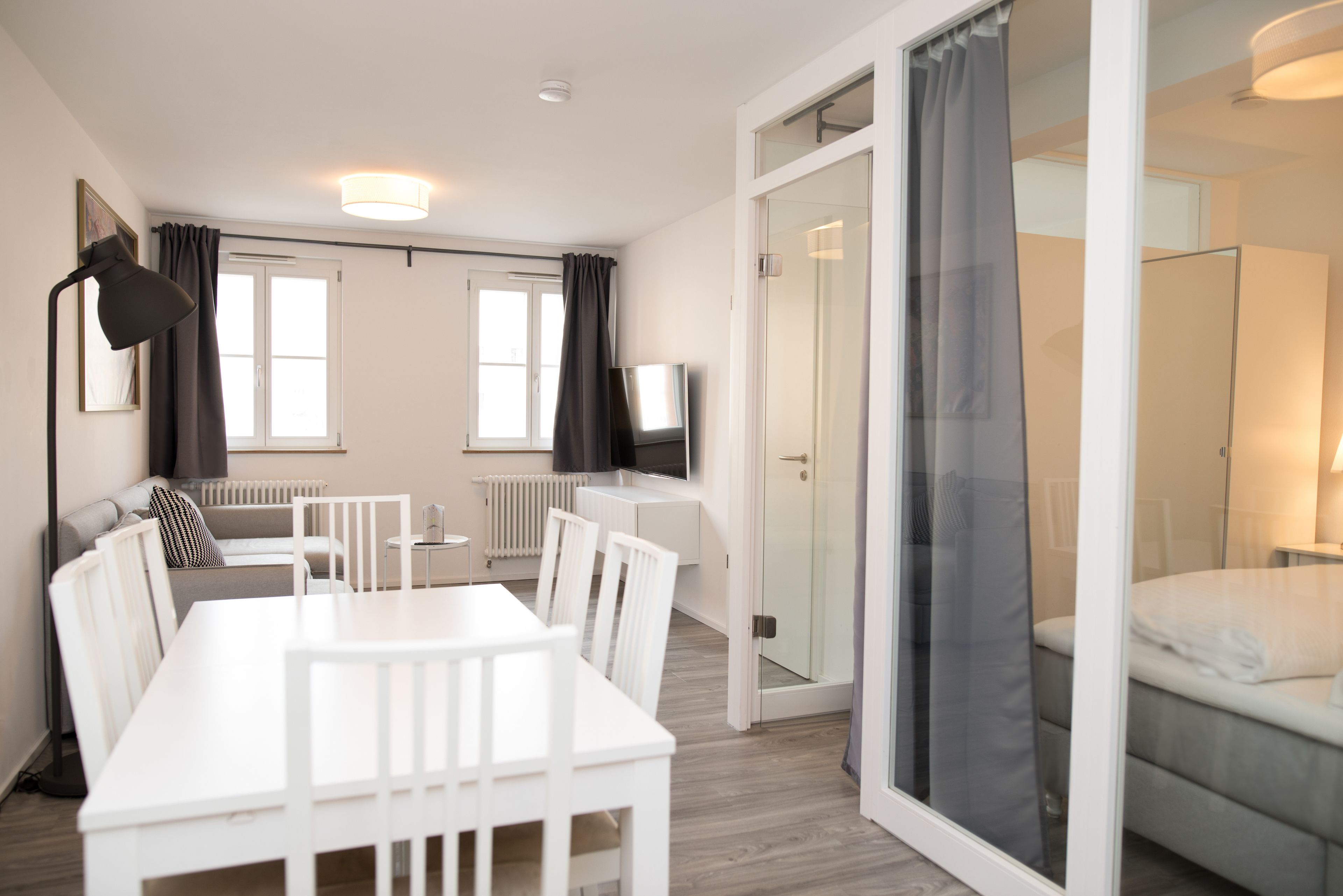 A modern hotel room with a dining area, a TV, and a sliding glass door leading to a balcony.