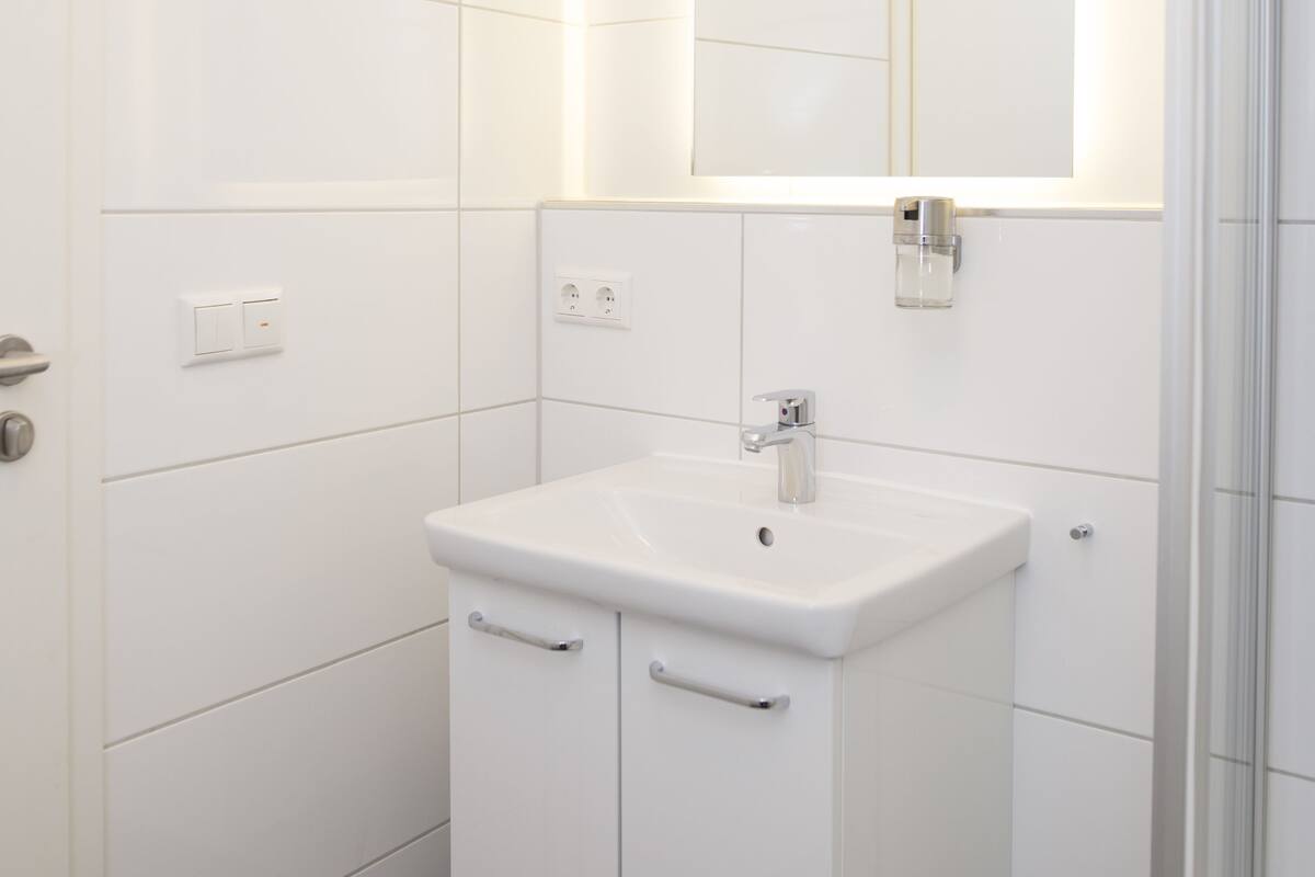 A modern bathroom with a white vanity, a mirror, and a shower area.