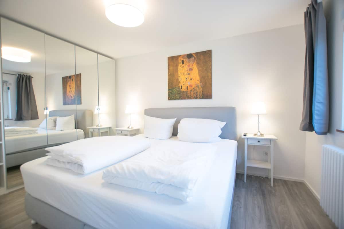 A hotel room with a large bed, two bedside tables with lamps, a mirror, and a painting on the wall.