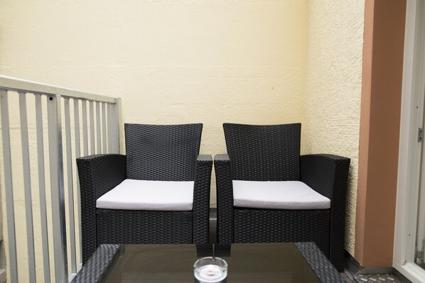 Un petit espace extérieur aménagé avec deux fauteuils en osier et une table, agrémenté d’un porte-bougie en verre.