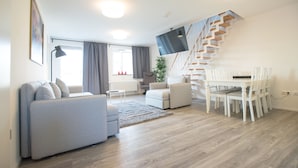 A modern living room with a staircase, a dining area, and a flat-screen TV mounted on the wall. - Arnulfsplatz Aparts (Regensburg)