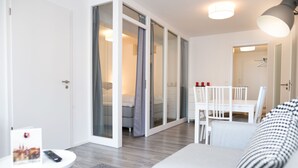 A modern hotel room with a sofa, a small table, and a dining area with chairs. - Arnulfsplatz Aparts (Regensburg)