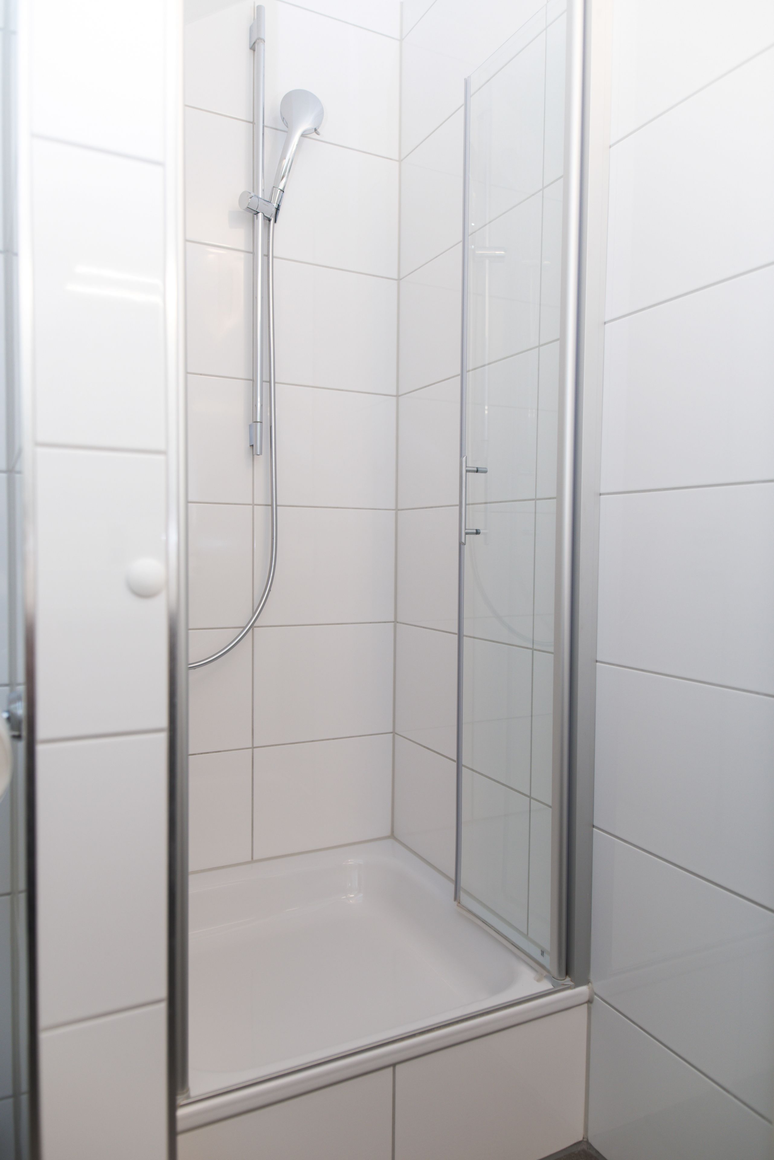Cabina de ducha con paredes de vidrio, azulejos blancos y ducha de acero cromado.
