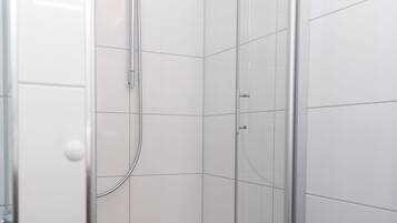 Cabina de ducha con paredes de vidrio, azulejos blancos y ducha de acero cromado.