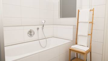 A modern bathroom with a white bathtub, a wooden towel rack, and a mirror above the tub.